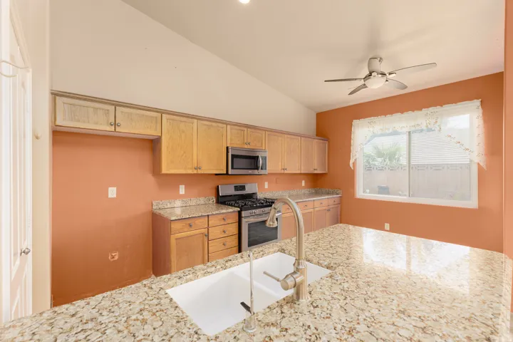 Kitchen featuring granite countertops, wood cabinetry, stainless steel appliances, and a vaulted ceiling