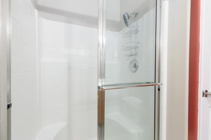 Shower enclosure with a clear glass sliding door, white tiled walls, and a built-in shower bench