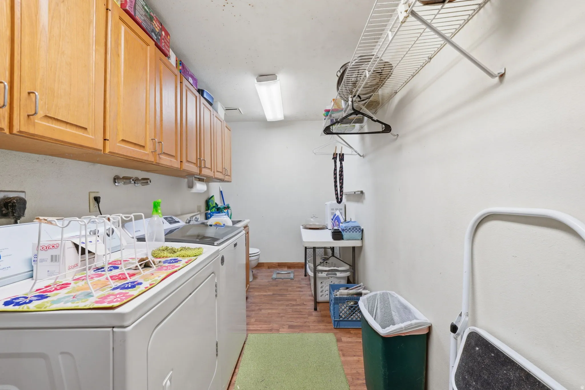 Laundry area featuring wood-finish flooring, overhead cabinetry, a utility sink, and wall-mounted shelving