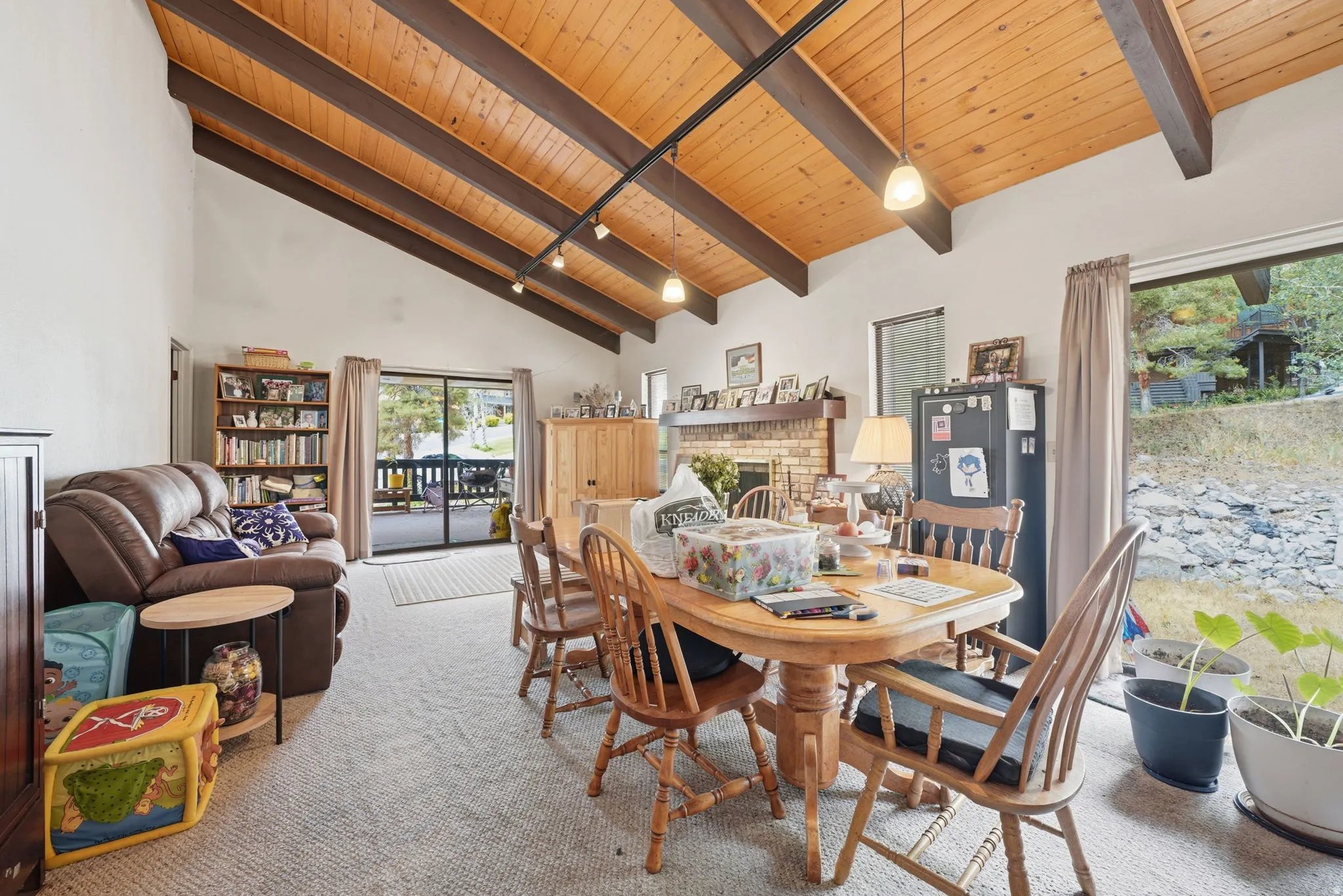 Vaulted wood-plank ceiling with exposed beams, track lighting, brick fireplace, and sliding glass door