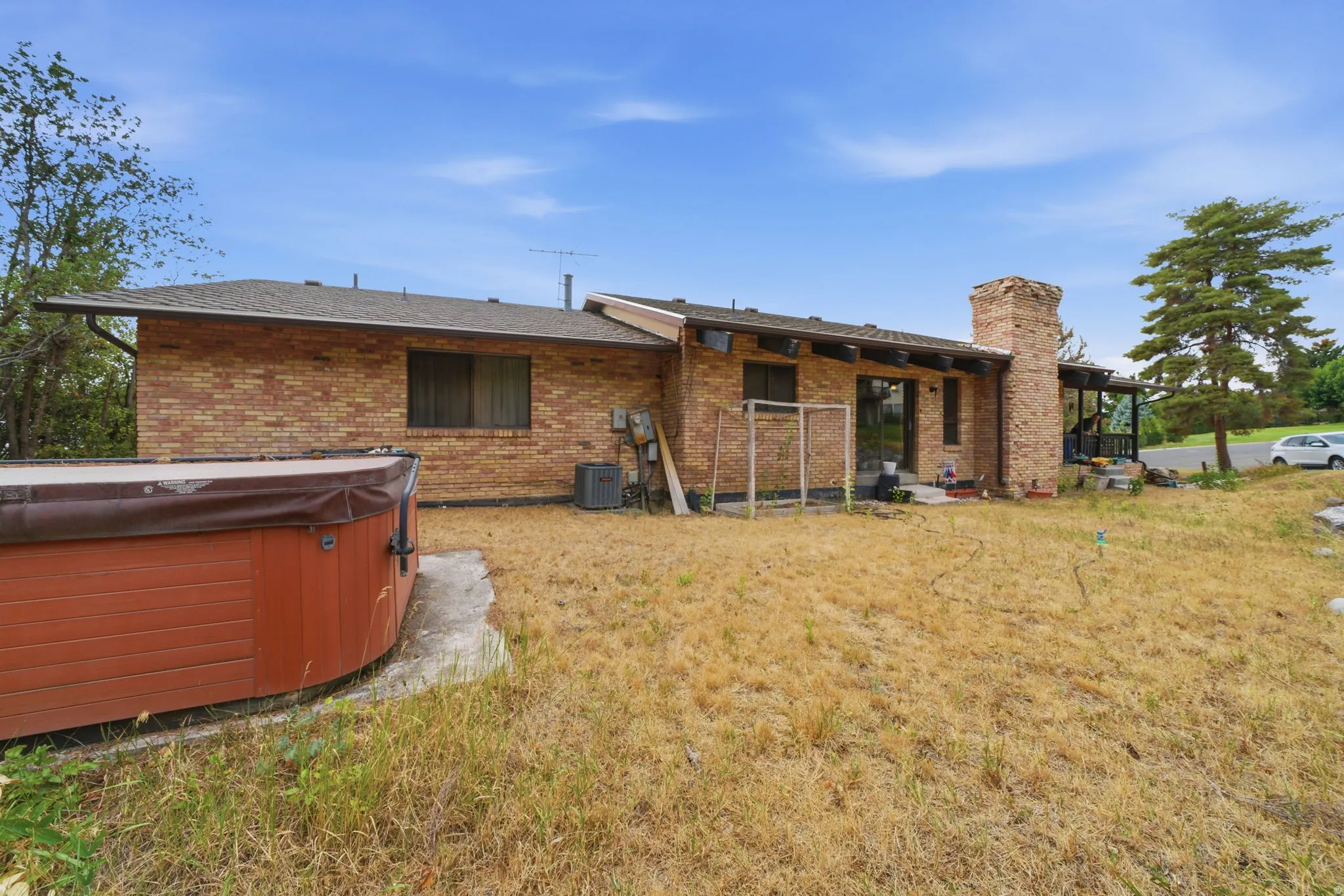 Brick exterior with a prominent brick chimney, covered patio, and a hot tub