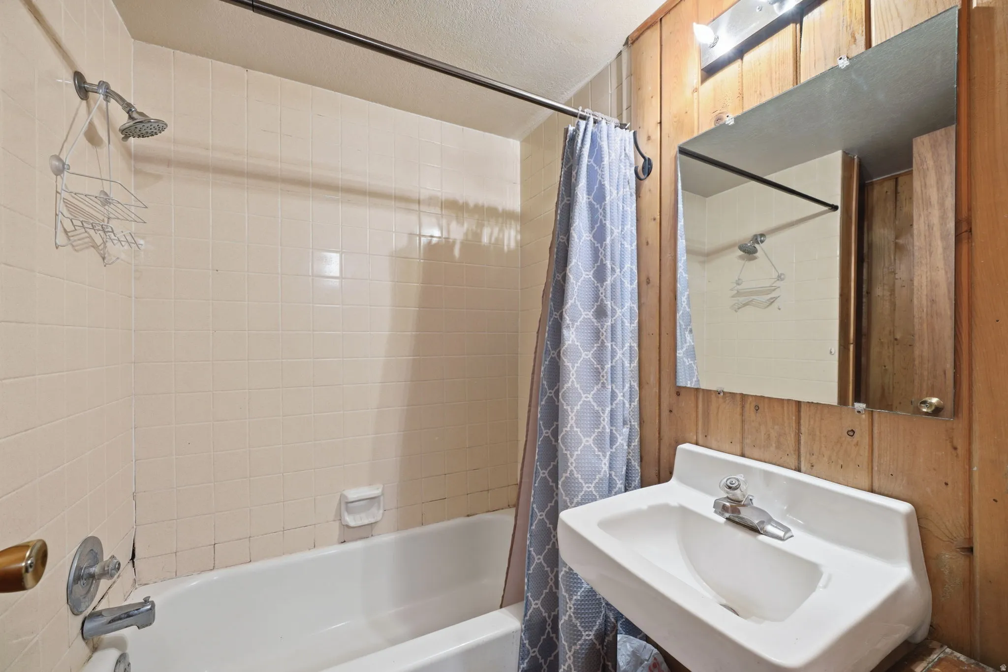 Bathtub with tile surround, wall-mounted sink, wall-mounted mirror, and wood-paneled wall