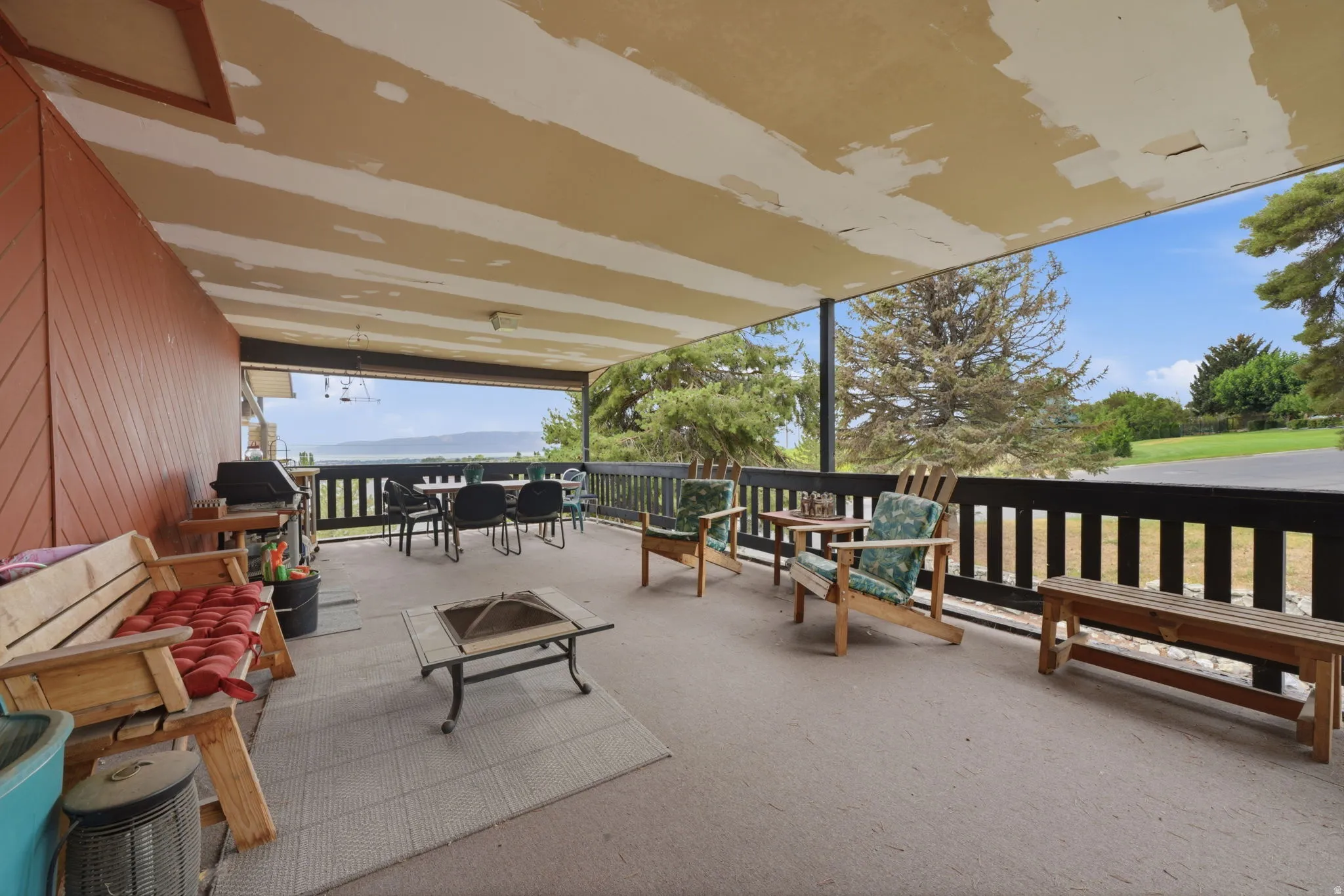 Expansive covered patio with a dark wood-tone railing and a scenic water backdrop