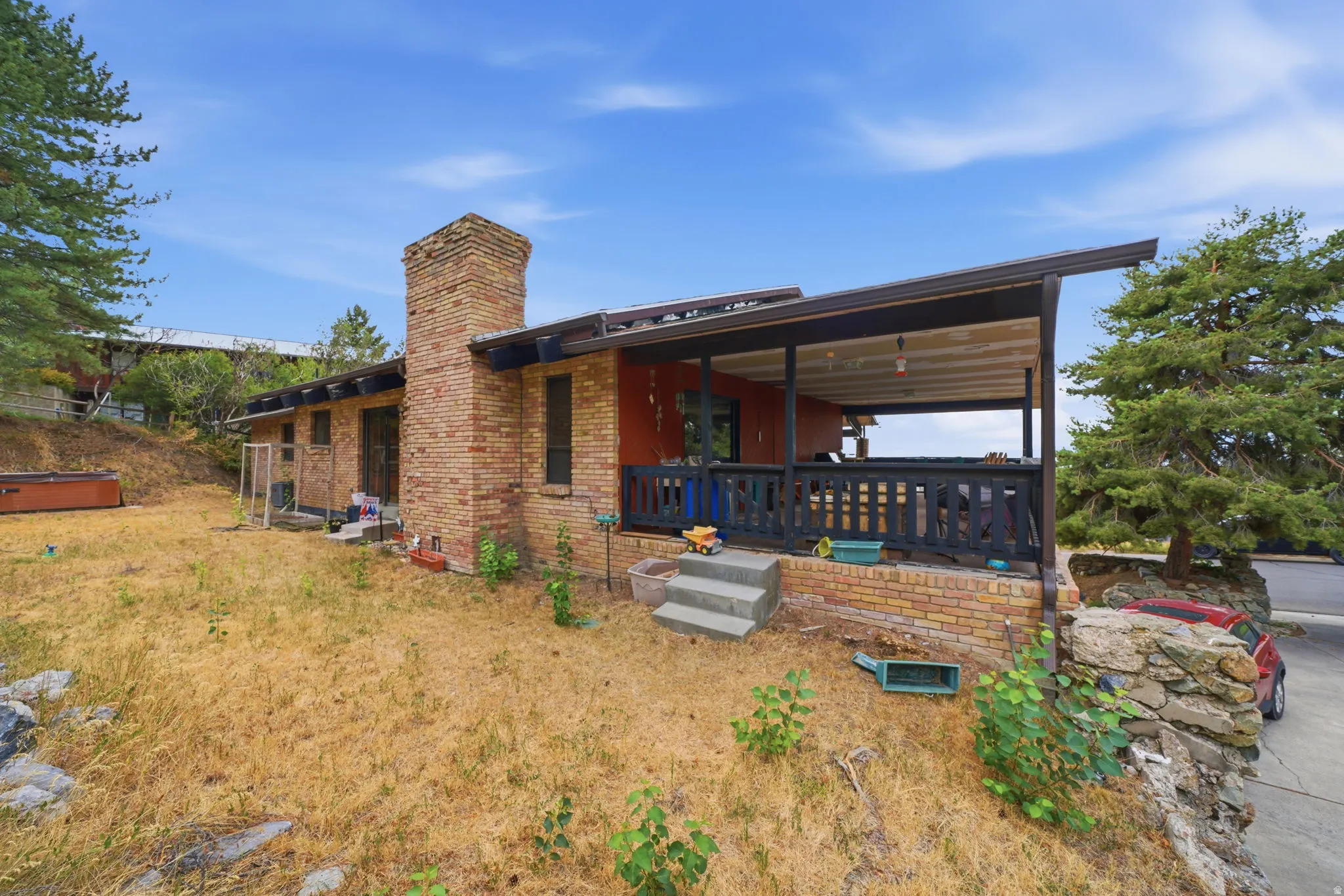 Brick exterior with an integrated chimney, an elevated covered porch with a dark railing, and concrete steps