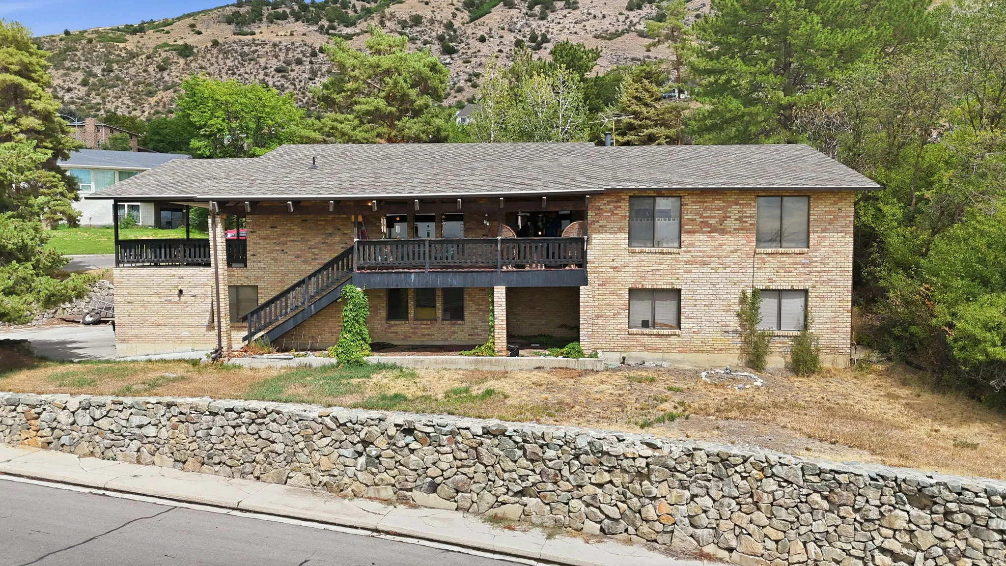 Brick exterior with multiple windows, covered balcony, exterior staircase, and stone retaining wall