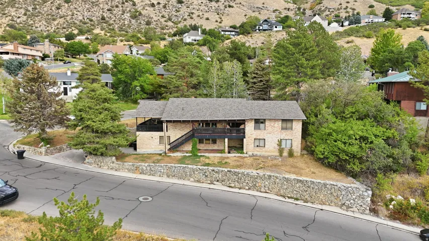 Brick exterior with a multi-level deck, dark shingle roof, and a stone retaining wall