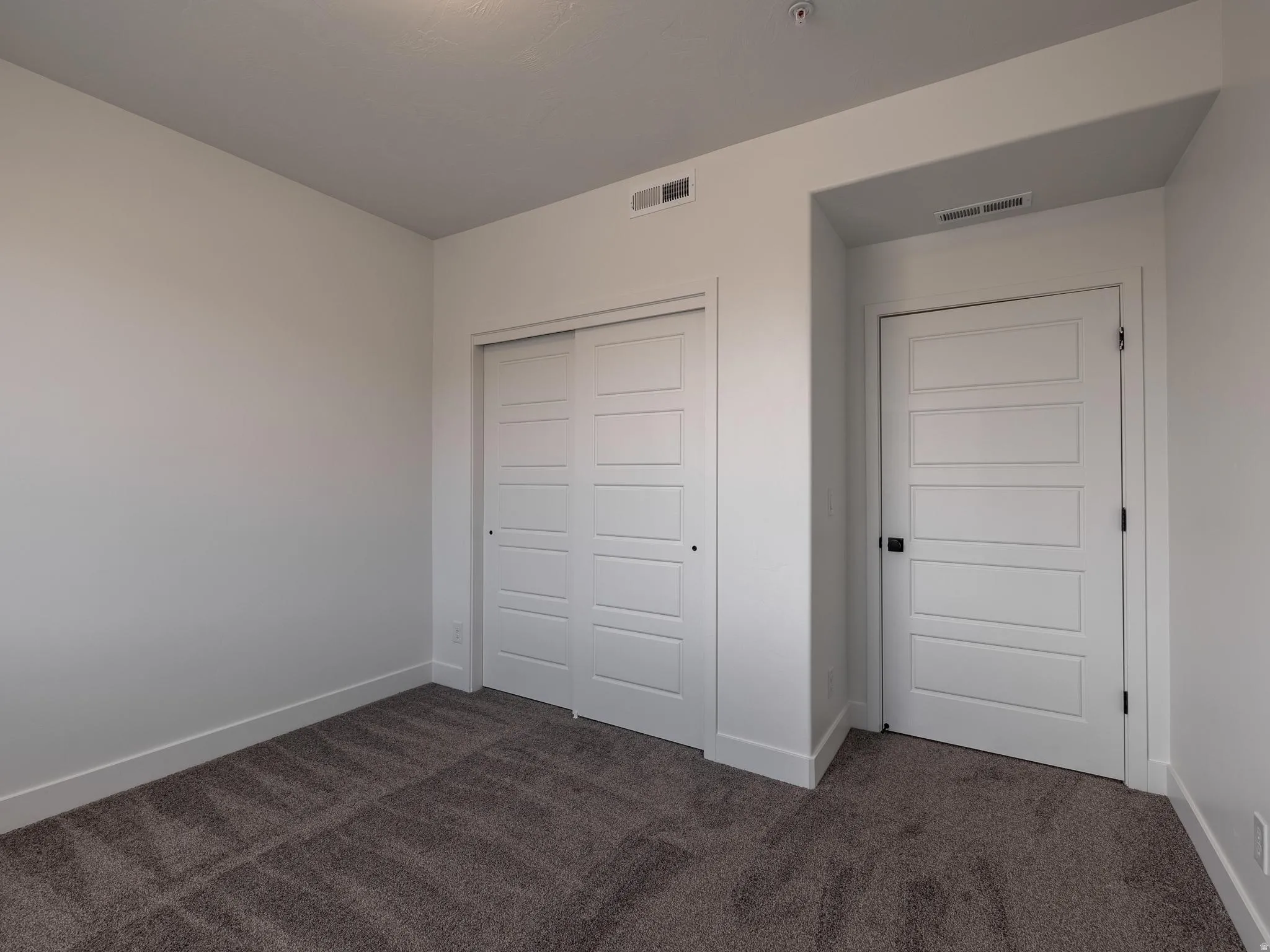 Neutral wall paint, textured carpet flooring, white trim, sliding panel closet doors, and a solid panel door with black hardware