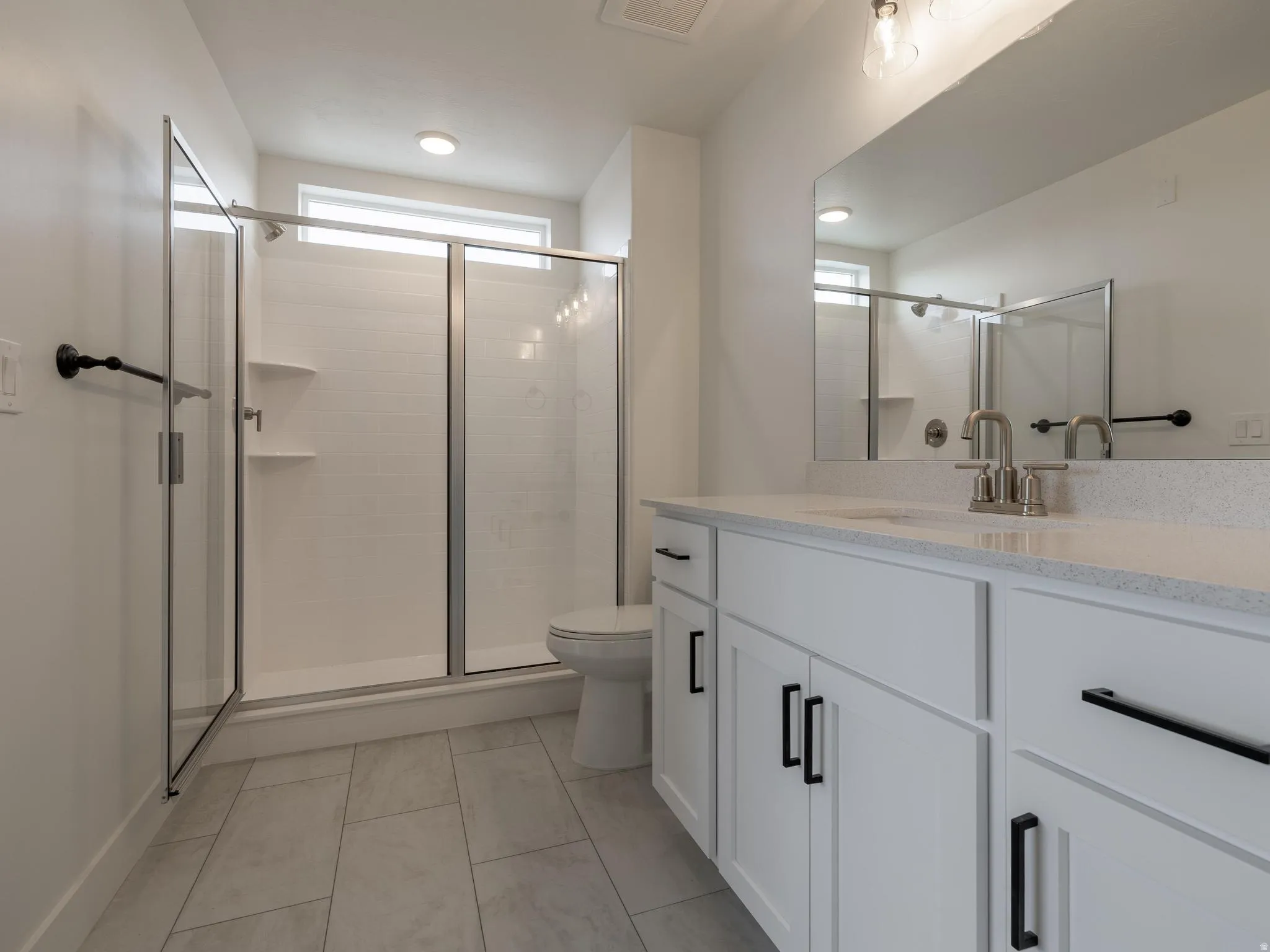 White shaker cabinetry with black hardware, double vanity with light-colored countertop, and a walk-in shower with glass enclosure
