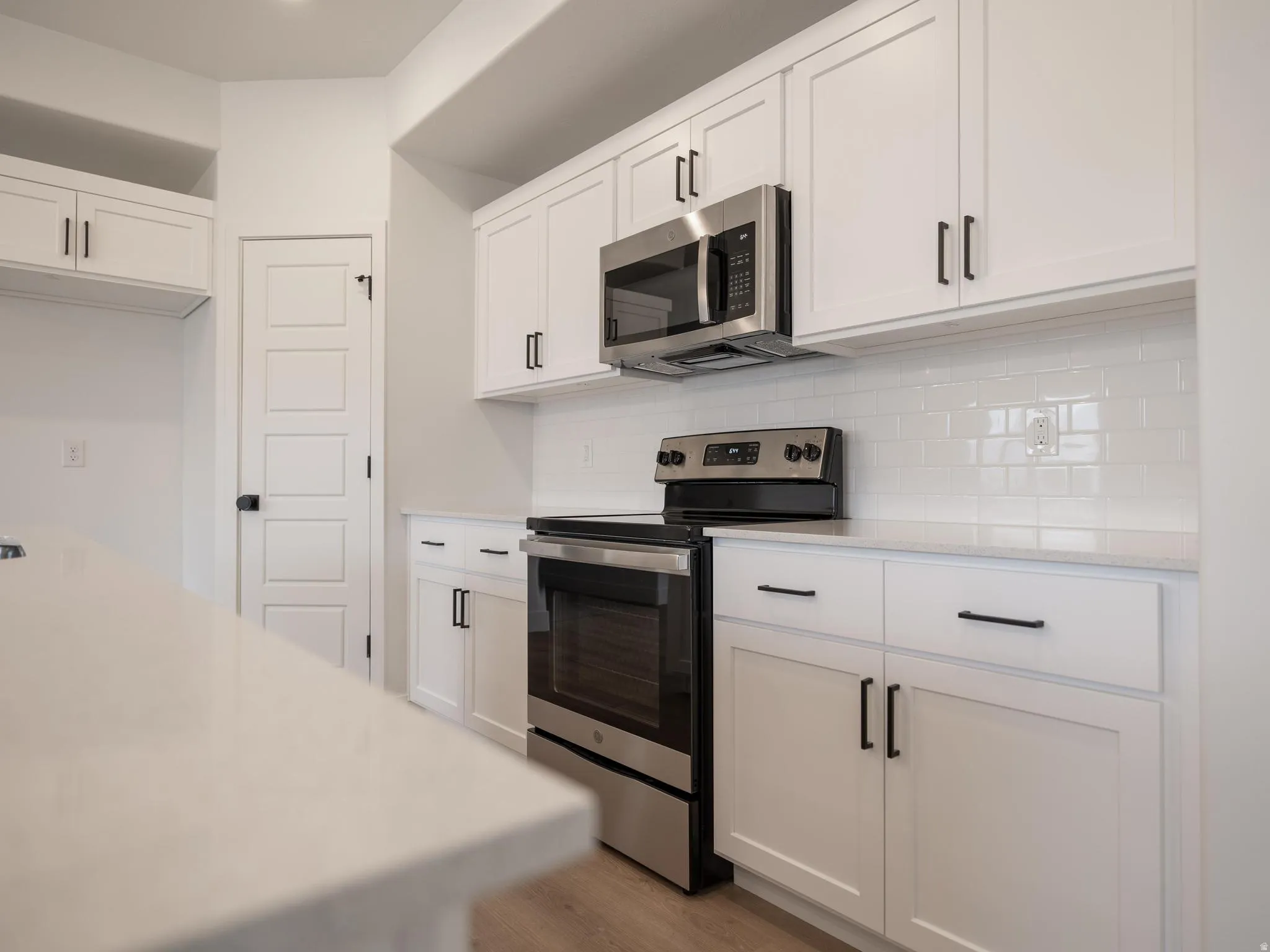 White shaker-style cabinetry with black hardware, stainless steel appliances, white subway tile backsplash, and light-toned countertops