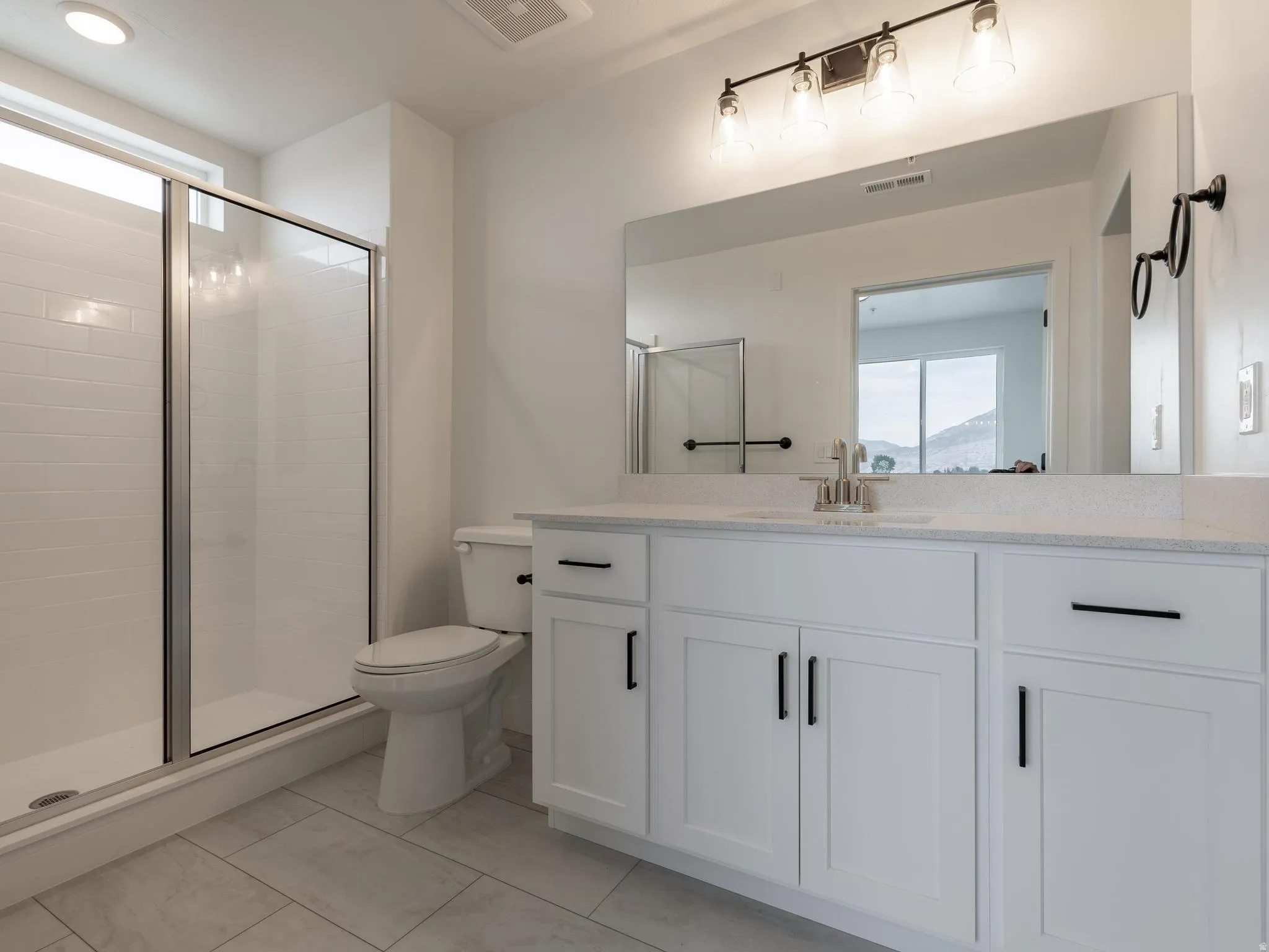 White shaker-style cabinetry with black hardware, extended vanity countertop, and a walk-in shower with clear glass enclosure