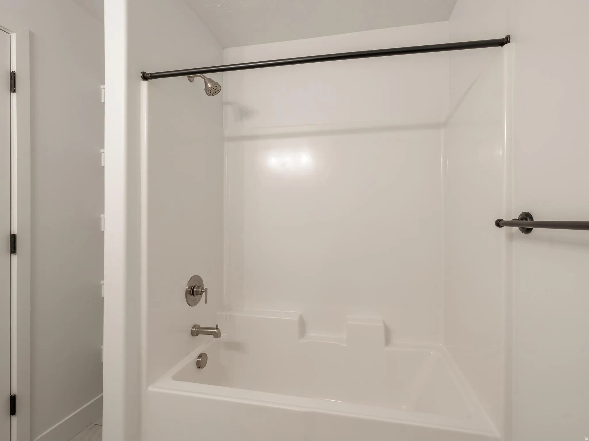 White bath and shower combination unit featuring a brushed nickel shower head and tub filler