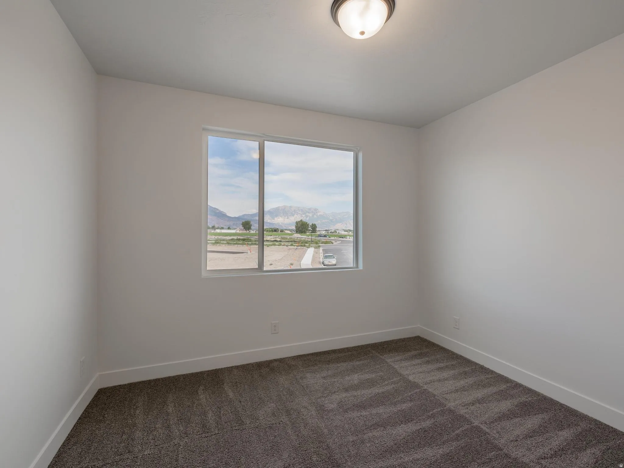 Spacious room with plush gray carpeting, neutral wall color, contemporary flush-mount light fixture, and a large window offering mountain scenery