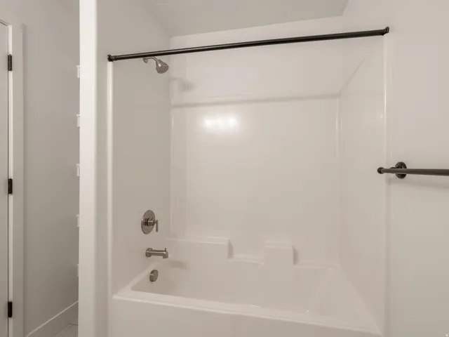 White bath and shower combination unit featuring a brushed nickel shower head and tub filler