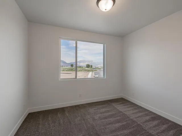 Spacious room with plush gray carpeting, neutral wall color, contemporary flush-mount light fixture, and a large window offering mountain scenery