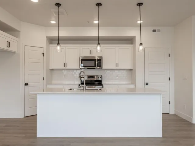 Kitchen featuring an island with a built-in sink, stainless steel appliances, white subway tile backsplash, white cabinetry with dark hardware, and wood-finish flooring