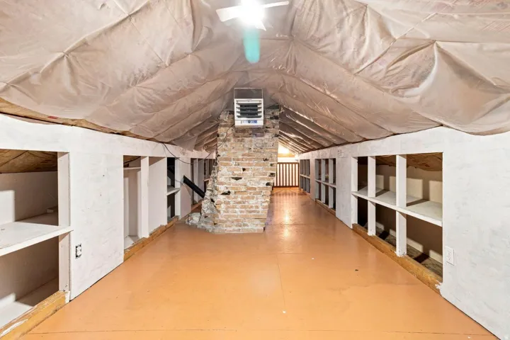 Attic space featuring exposed brick, built-in shelving, painted flooring, and overhead lighting
