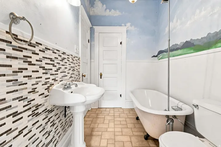 Spa-inspired bathroom featuring a freestanding soaking tub, pedestal sink, and custom tile work with a geometric brick pattern in neutral tones
