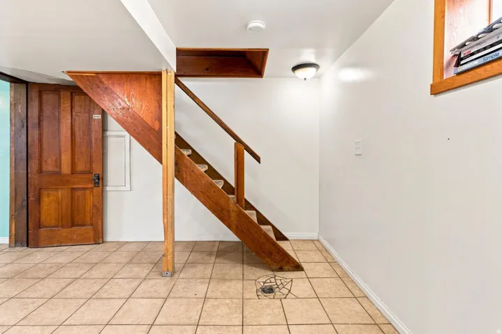 Wood-finish staircase with railing, panel door with dark hardware, recessed ceiling light, and ceramic tile flooring