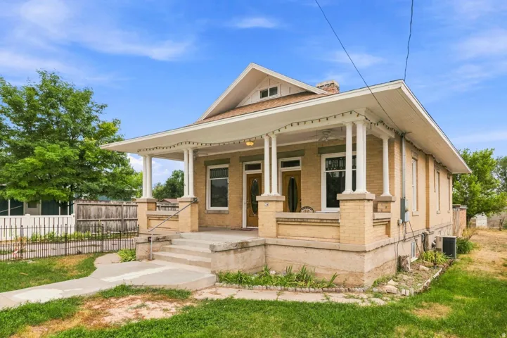 Brick exterior with a covered front porch, concrete steps, and a decorative wrought iron fence