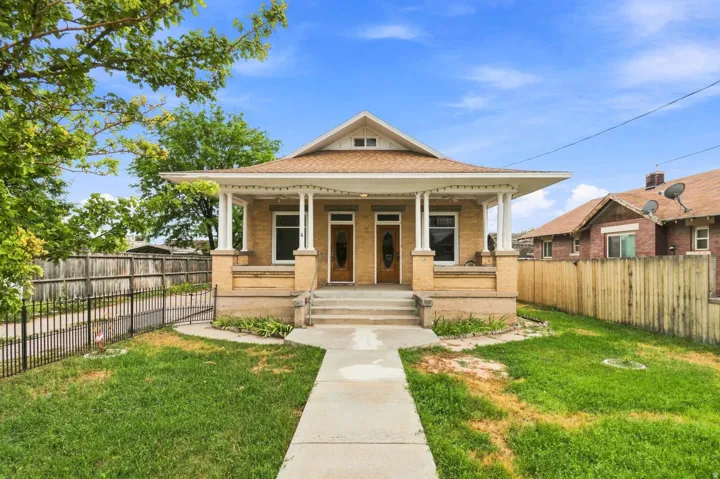 Brick exterior featuring a covered porch, dual entry doors, and a partial black metal fence