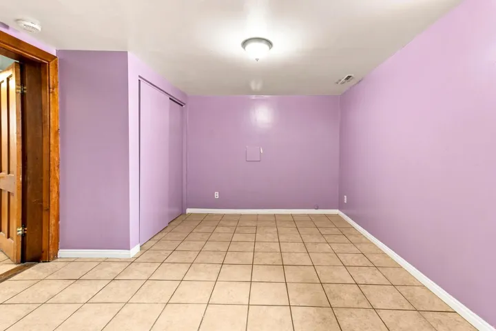 Spacious room featuring vibrant lavender walls, neutral tile flooring in a grid pattern, recessed ceiling lighting, and a wooden-finish entry door