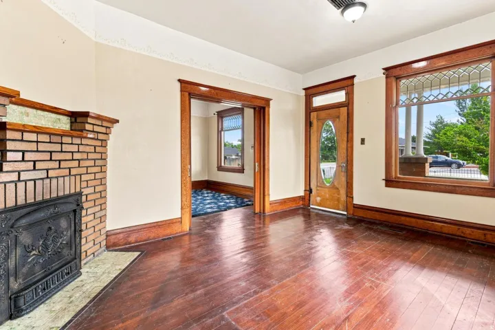 Hardwood flooring, brick fireplace with decorative insert, substantial wood trim, wood-paneled door with oval glass insert, and a transom window