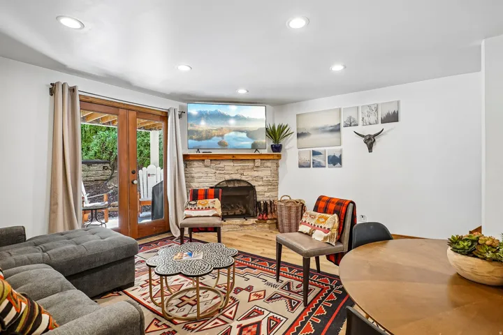 Stone-clad fireplace with a wood mantel, wood-finish flooring, recessed lighting, and double glass panel doors