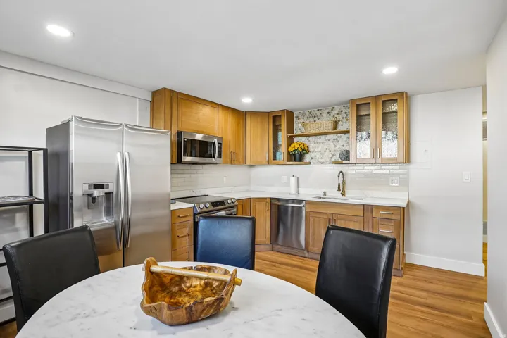 Kitchen featuring wood cabinetry, stainless steel appliances, white subway tile backsplash, and light-toned countertops
