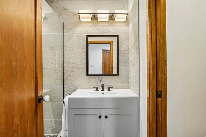 Bathroom featuring a gray vanity with an integrated sink, matte black faucet, framed mirror, and rectangular wall-mounted light fixture