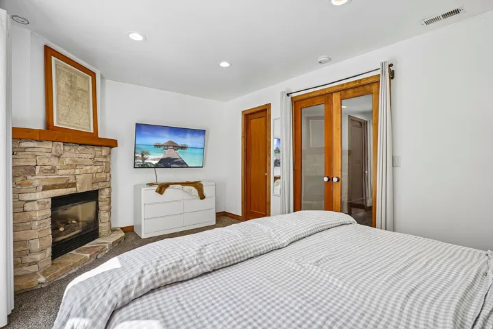 Stone fireplace with a wood mantle, recessed lighting, and wood-framed glass doors