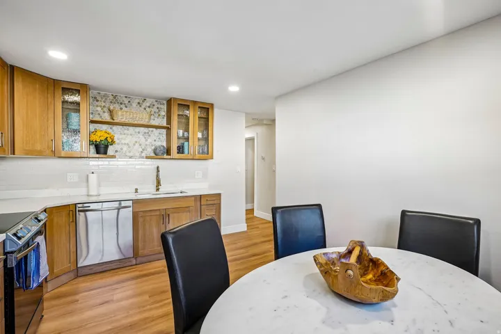 Kitchen featuring wood cabinetry with glass-front uppers, stainless steel dishwasher, white subway tile backsplash, and light countertops