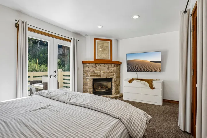 Stone-clad fireplace with wood mantle, French doors to a private balcony, recessed lighting, and soft carpet flooring
