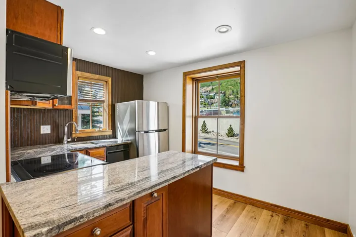Kitchen featuring rich wood cabinetry, stainless steel appliances, speckled stone countertops, and wood-finish flooring