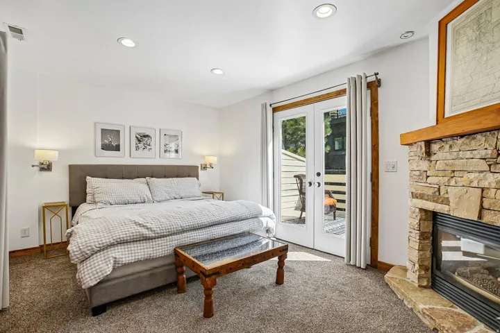 Stone-surround fireplace with hearth, recessed lighting, wall-mounted sconces, and double French doors opening to an outdoor area