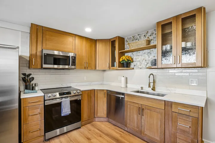 Kitchen featuring wood-finish cabinetry, stainless steel appliances, white quartz countertops, and a subway tile backsplash