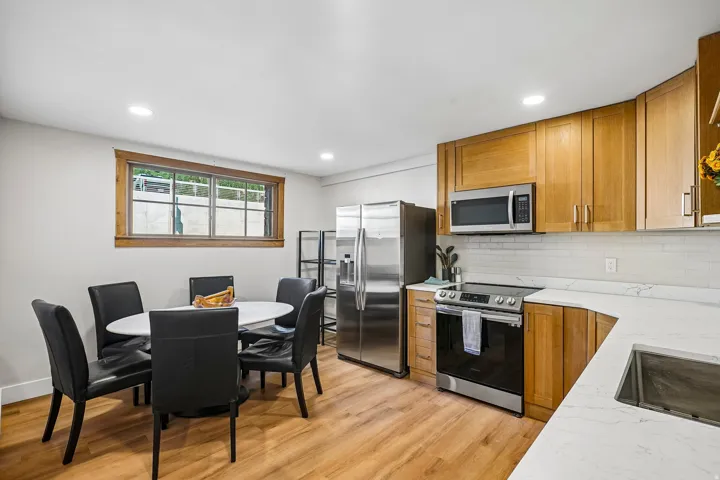 Kitchen area featuring wood-finish flooring, light wood cabinetry, white countertops, stainless steel appliances, and a tiled backsplash