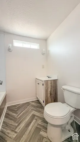 Bathroom featuring a vanity with a wood-finish cabinet and white countertop, white toilet, and herringbone pattern floor