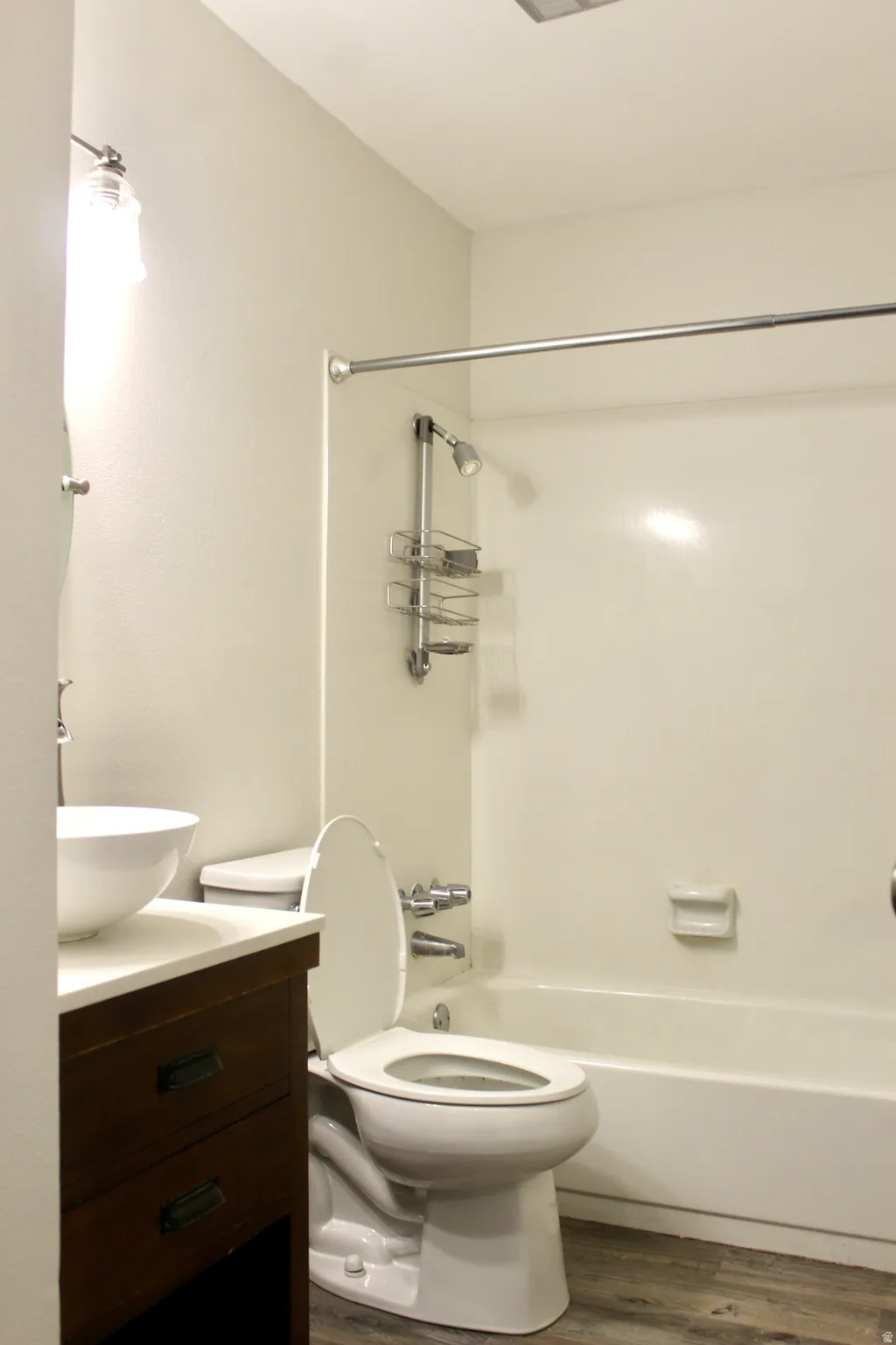 Bathroom featuring a white vessel sink, dark wood vanity with drawer pulls, a toilet, and a shower-over-tub combination with a wall-mounted showerhead and curtain rod