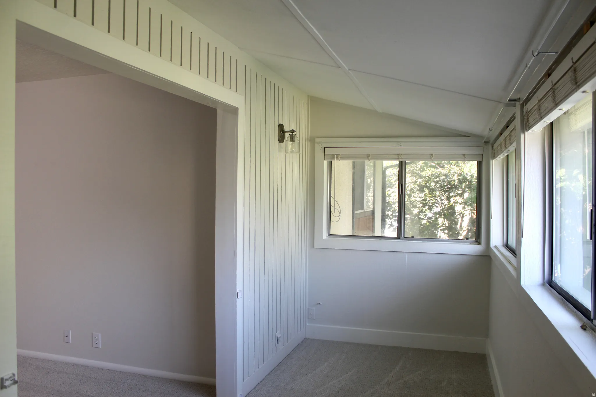 Carpeted room with multiple windows, an angled ceiling, and a wall-mounted light fixture