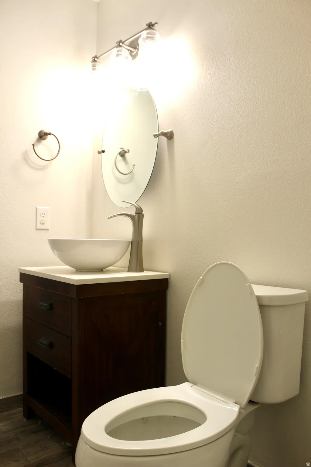 Vessel sink with a brushed nickel faucet, wood-finish vanity, white countertop, and wood-finish flooring