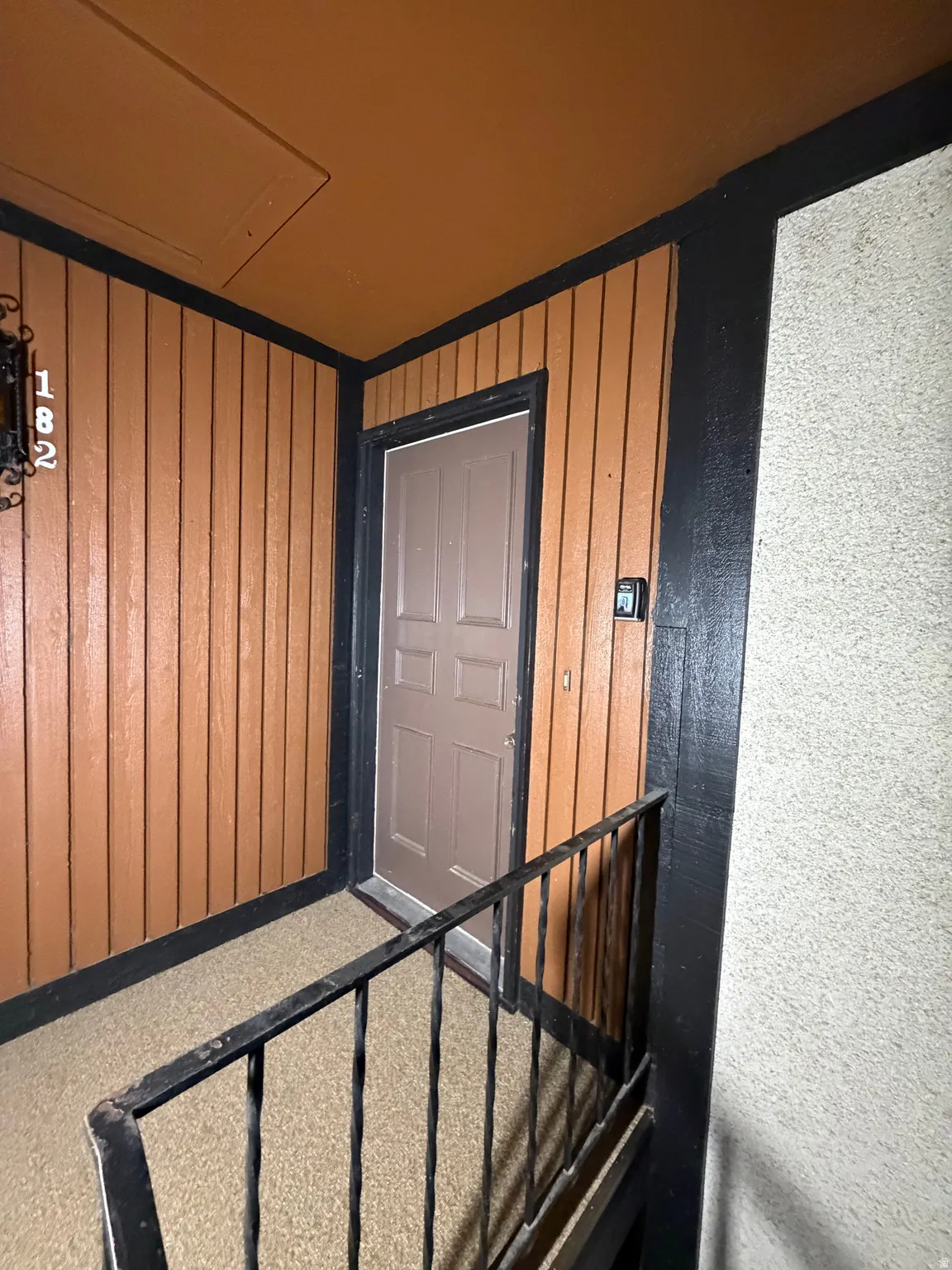 Entryway featuring vertical wood paneling, a panel door, black railings, and a granular textured floor