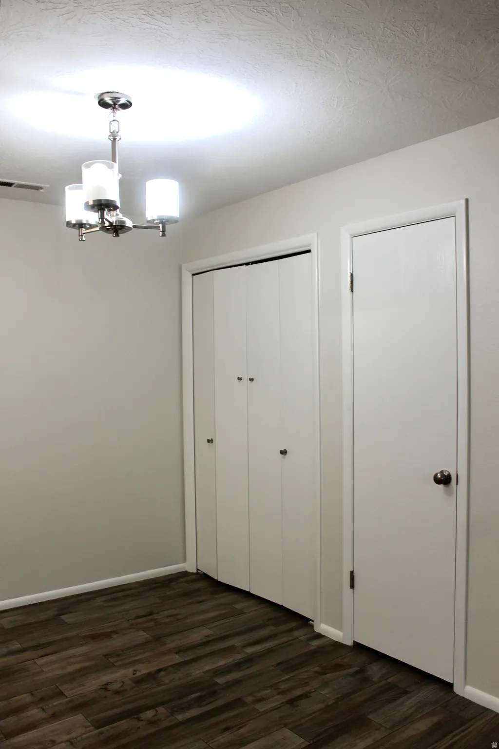 Wood-finish flooring, white walls, and a contemporary three-light chandelier