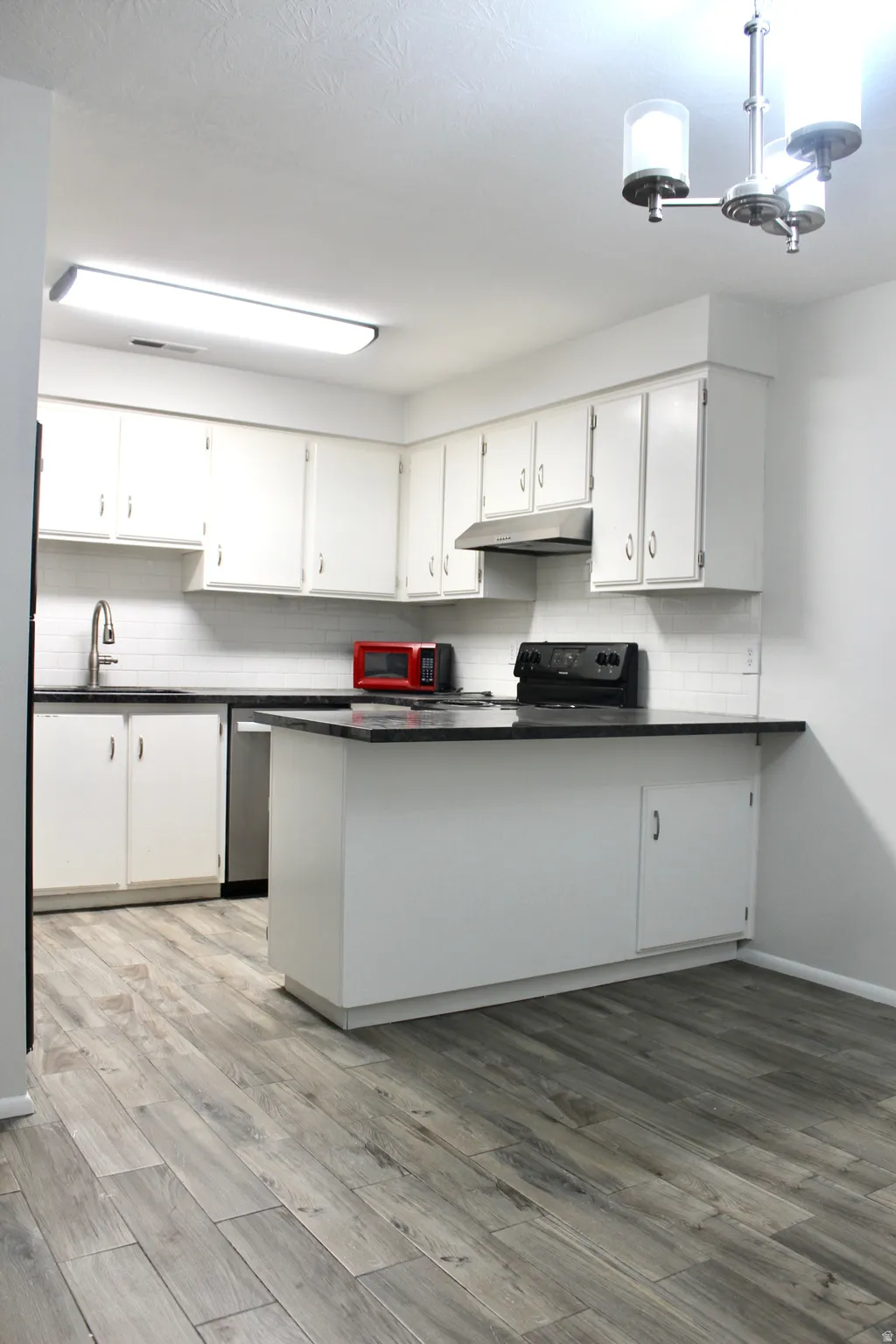 Kitchen featuring white cabinetry, dark countertops, white subway tile backsplash, and wood-finish flooring