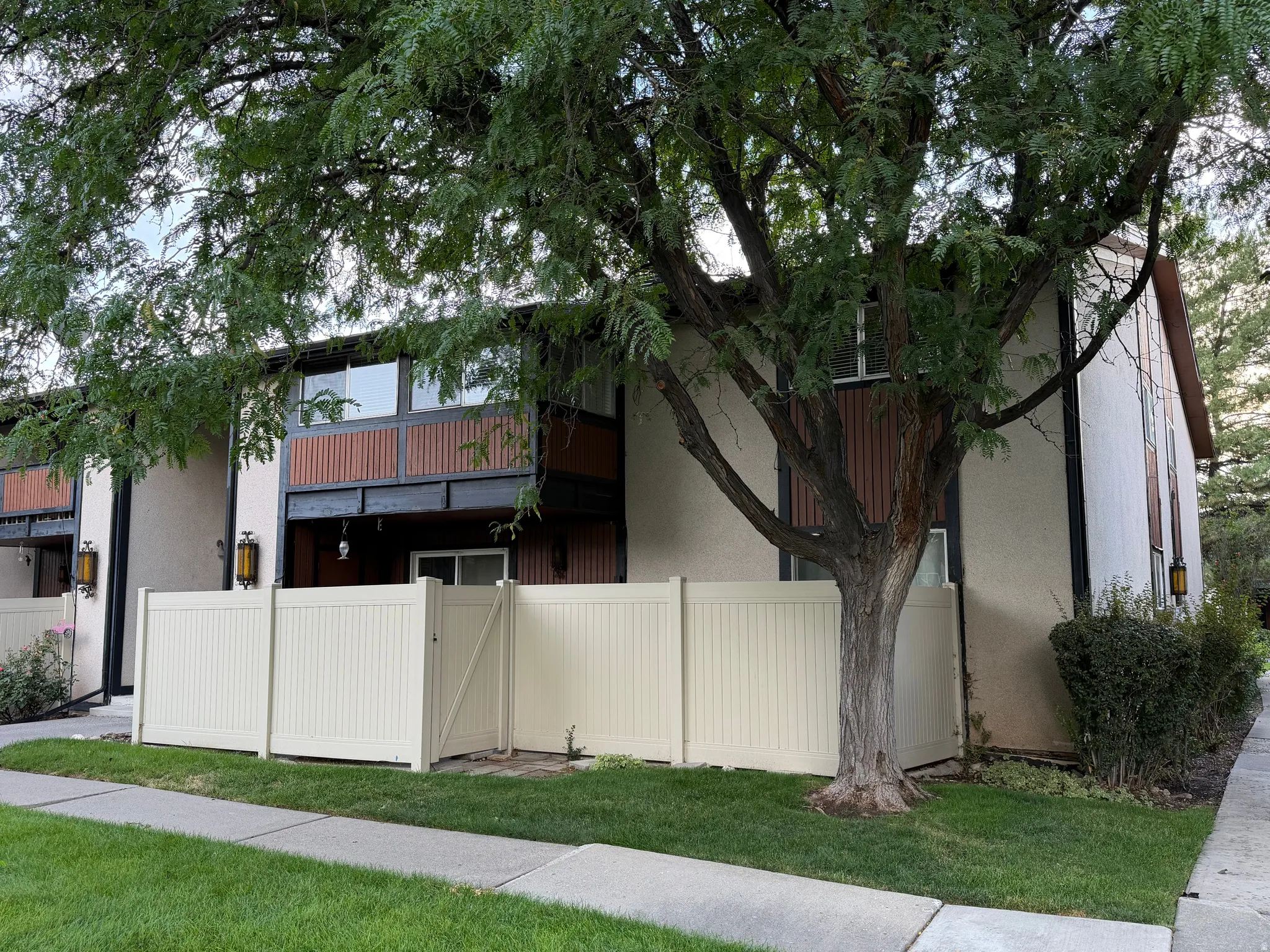 Fenced patio area with gate, mature tree, stucco exterior, and accent paneling