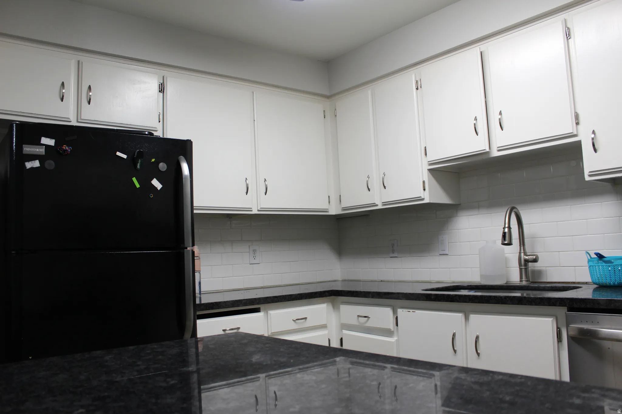 White shaker-style cabinetry, dark speckled countertops, subway tile backsplash, stainless steel kitchen sink, and a stainless steel pull-down faucet