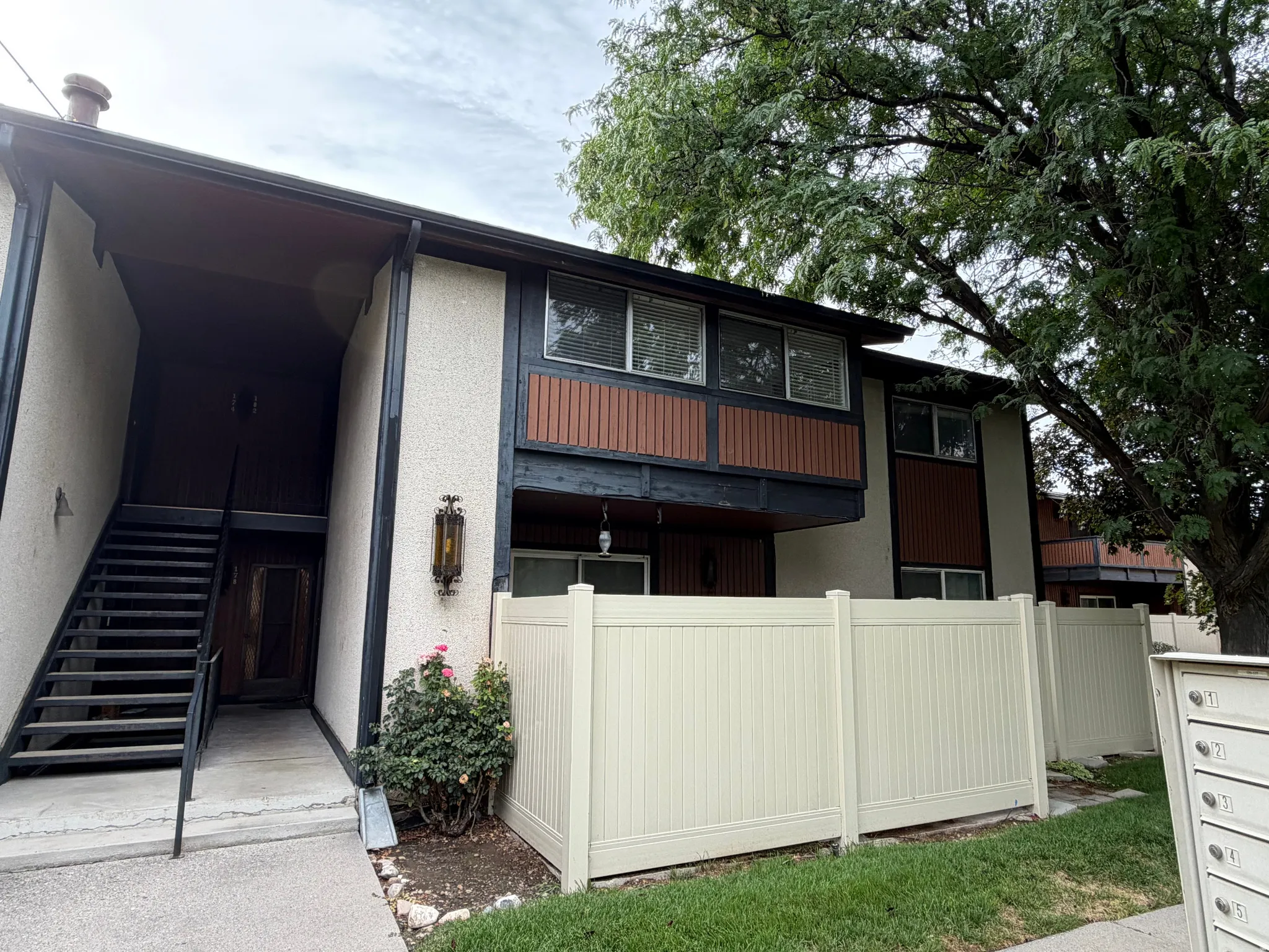 Exterior featuring stucco siding, brown accent panels, multiple windows, and a private staircase entry
