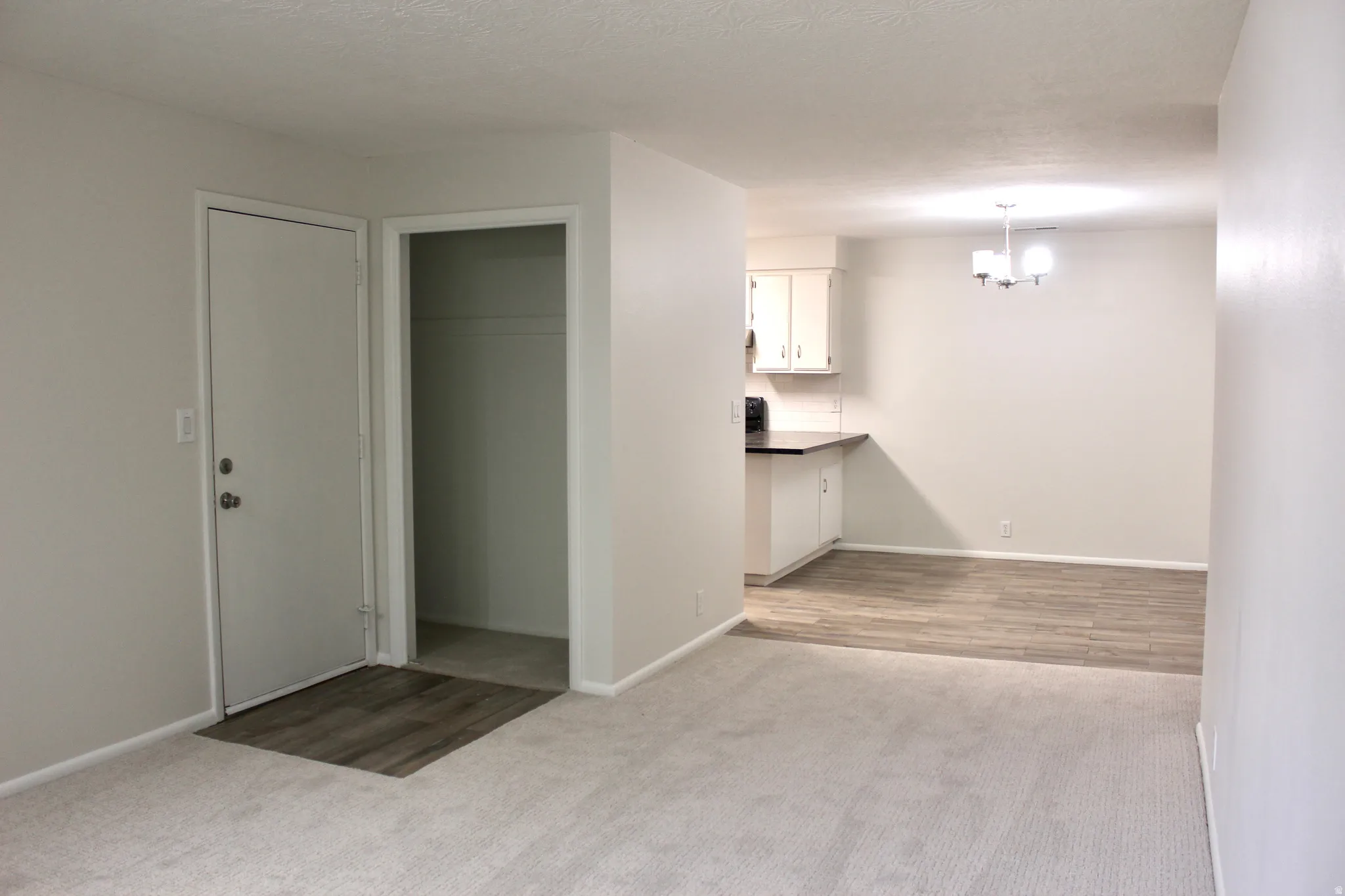 Neutral wall colors, carpet flooring, wood-finish flooring, white cabinetry, and a built-in chandelier