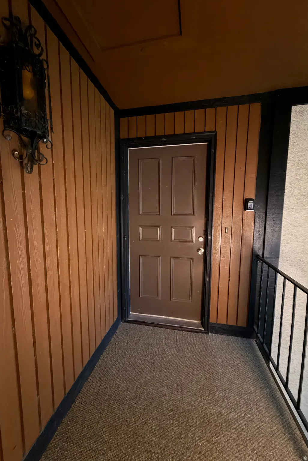 Brown paneled entry wall with black trim, dark brown door, and black metal railing