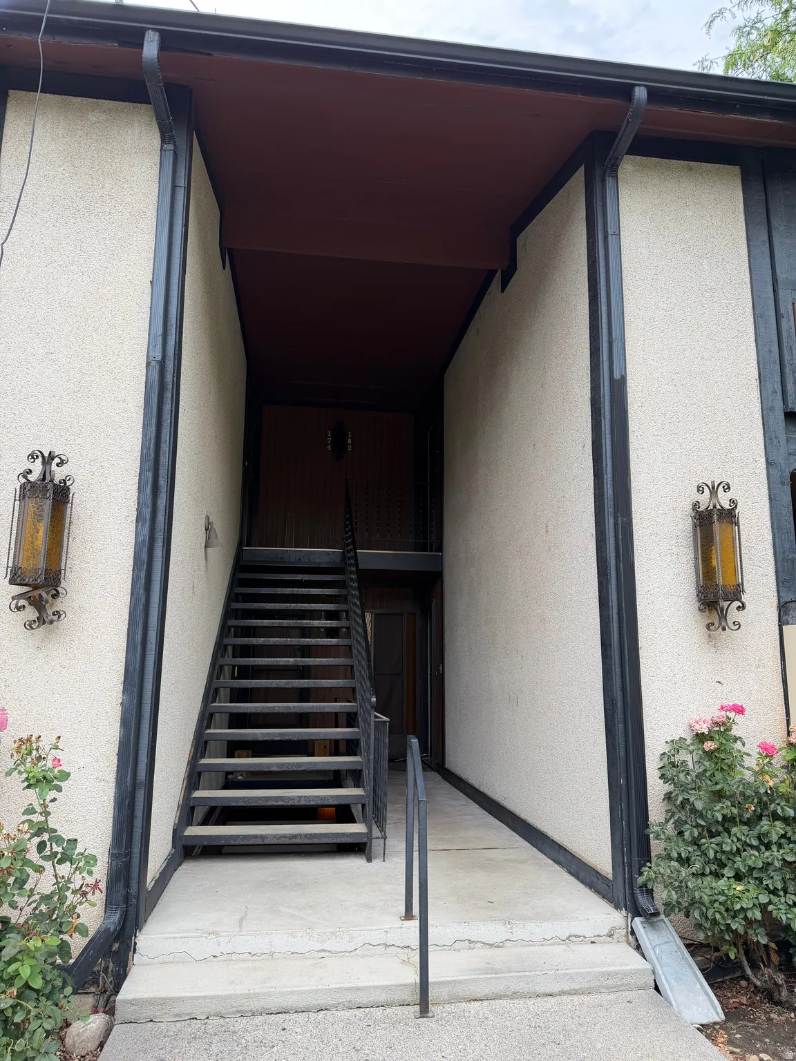 Exterior featuring textured stucco, black trim detailing, wrought iron wall sconces, and an exterior metal staircase