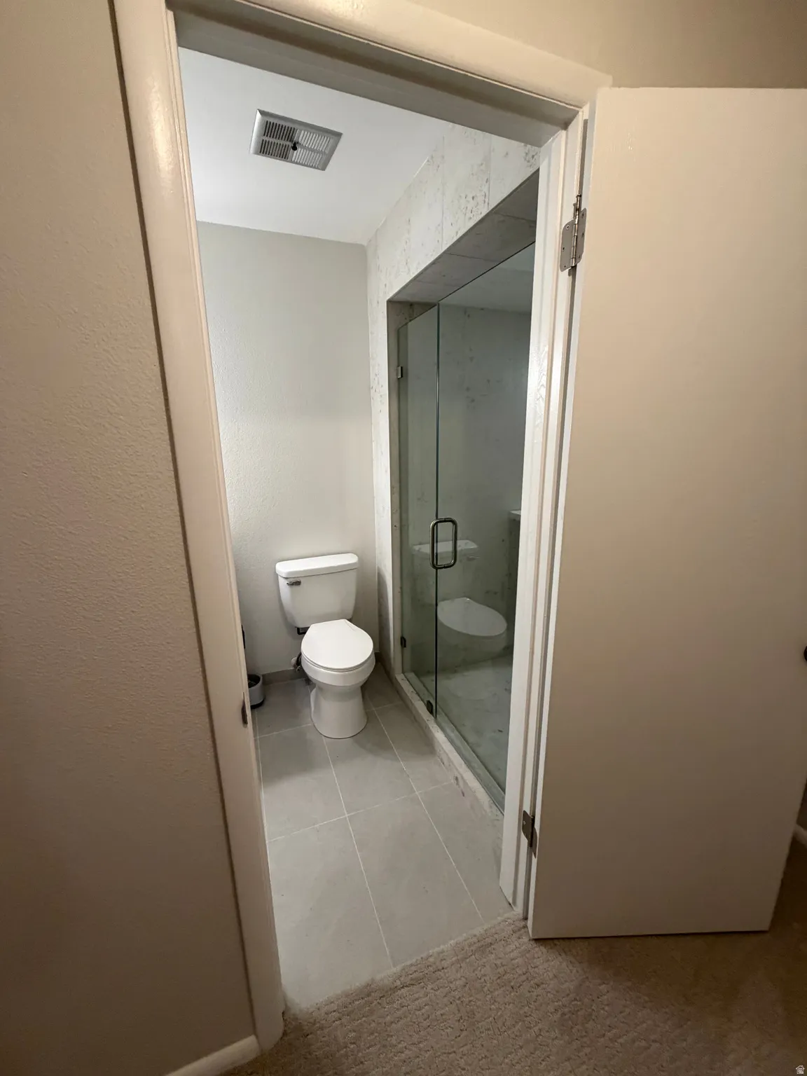 Modern bathroom featuring a sleek walk-in shower enclosure with frameless glass doors, ceramic tile flooring, recessed ceiling lighting, and a contemporary toilet fixture